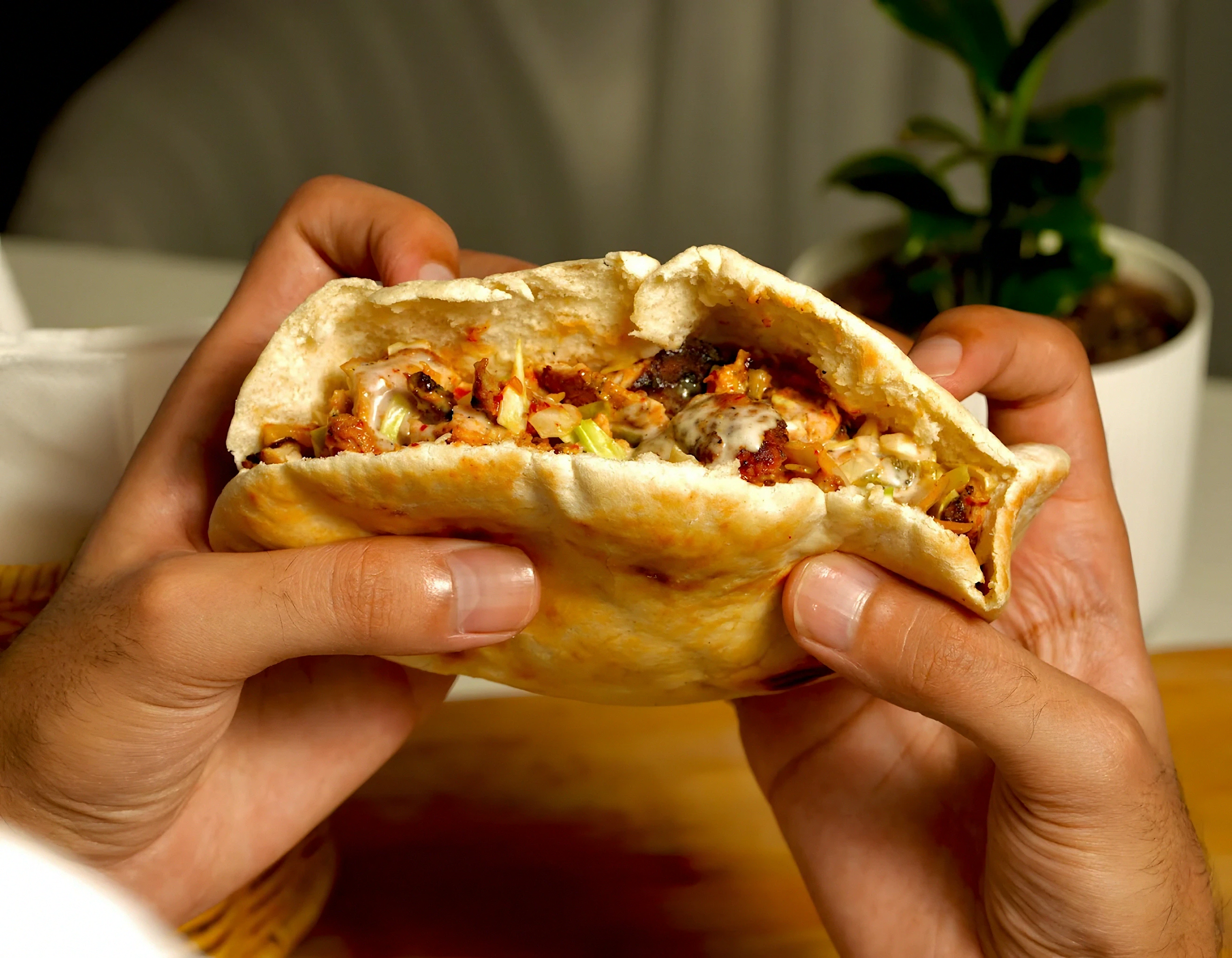 Two hands holding a stuffed chicken pita doner